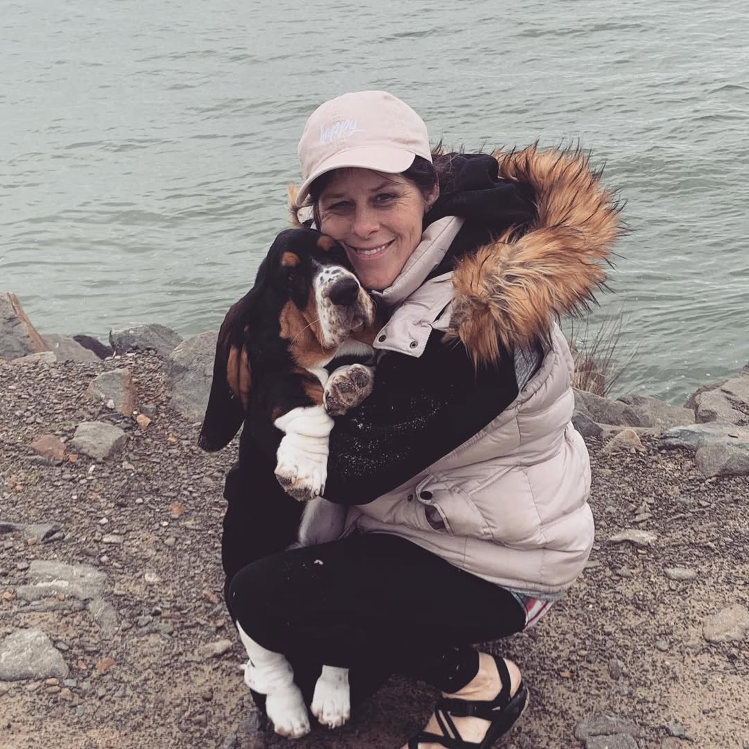 Person hugging a Basset Hound beside the water